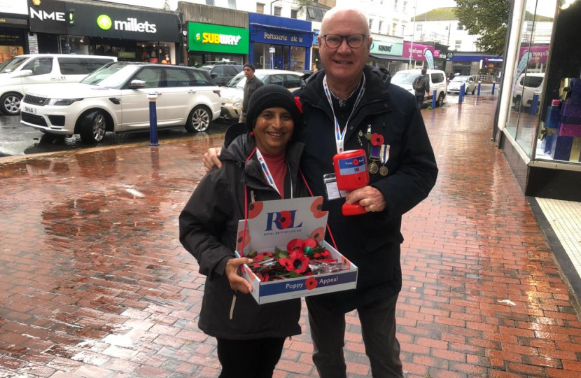 Cllr Kshama and Chairman Iain selling poppies in the rain. Smiling, looking happy.
