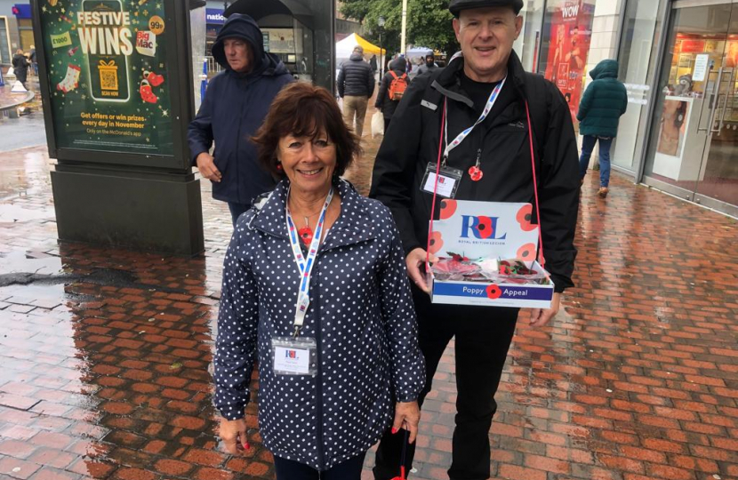 Volunteer Ruth with Cllr Nigel selling poppies in the rain. Smiling.