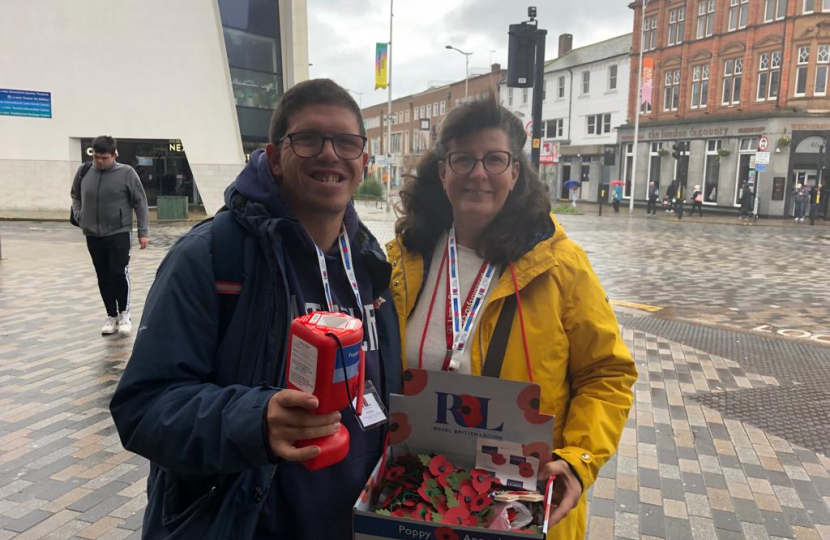 Benjamin and Sandra selling poppies in the rain. Both smiling, looking happy.