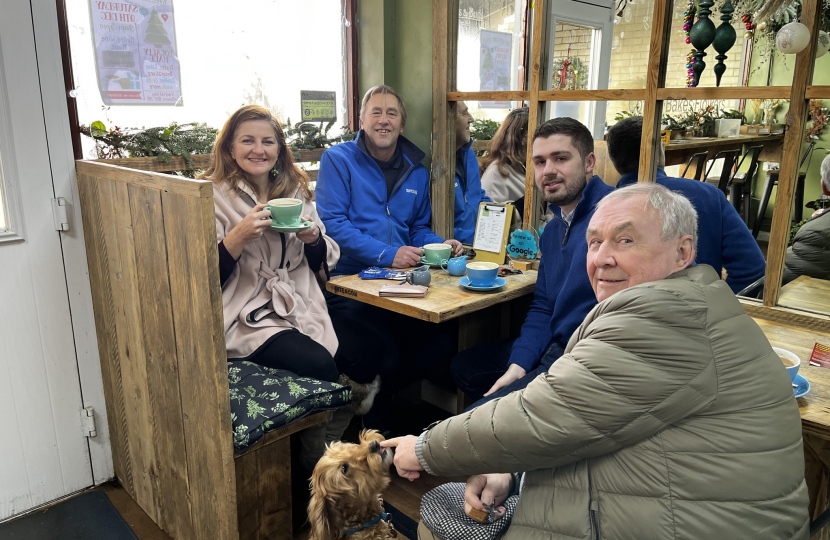 MP Caroline Ansell with Cllr, Colin Belsey, David Small and Nick Ansell. Seated at a table in Beans and Buds enjoying a coffee. There's a very cute puppy next to Colin.
